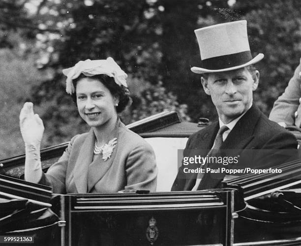 Queen Elizabeth II and Prince Philip, Duke of Edinburgh wave from the Royal Carriage as they arrive for a race meeting at Ascot Racecourse, England,...