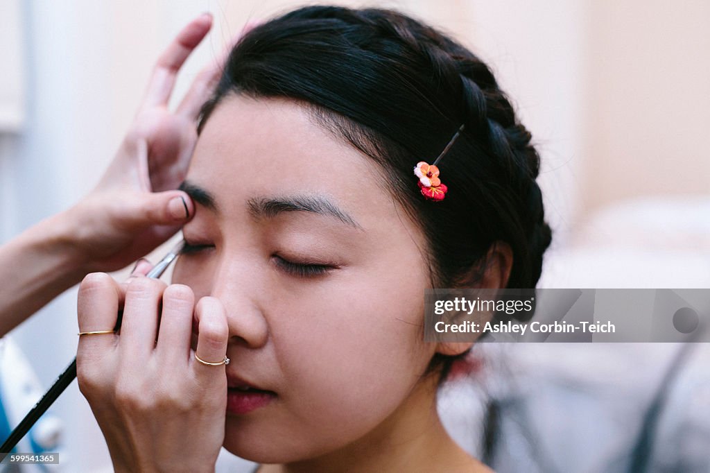 Hands of make up artist applying make up on young woman with eyes closed