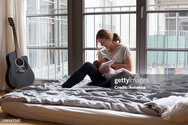 mother breastfeeding baby girl in bedroom - akustikgitarre stock-fotos und bilder