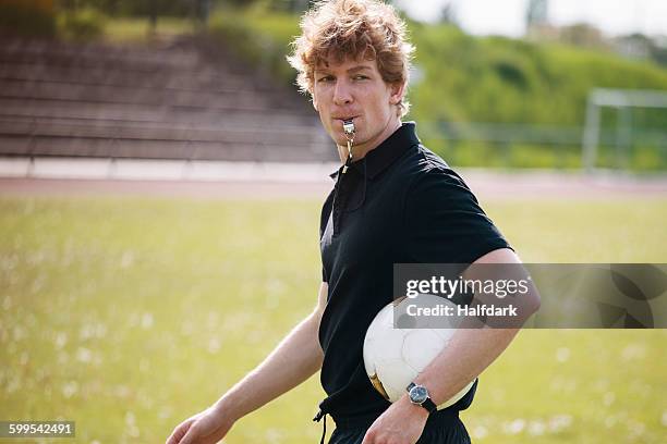 referee blowing whistle while carrying soccer ball on field - fluit sportartikelen stockfoto's en -beelden