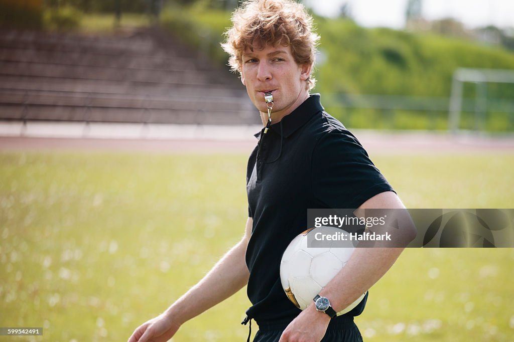 Referee blowing whistle while carrying soccer ball on field