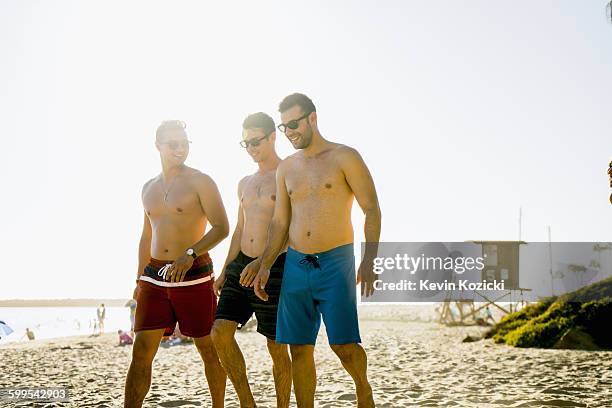 three young male friends strolling on newport beach, california, usa - swimwear stock-fotos und bilder