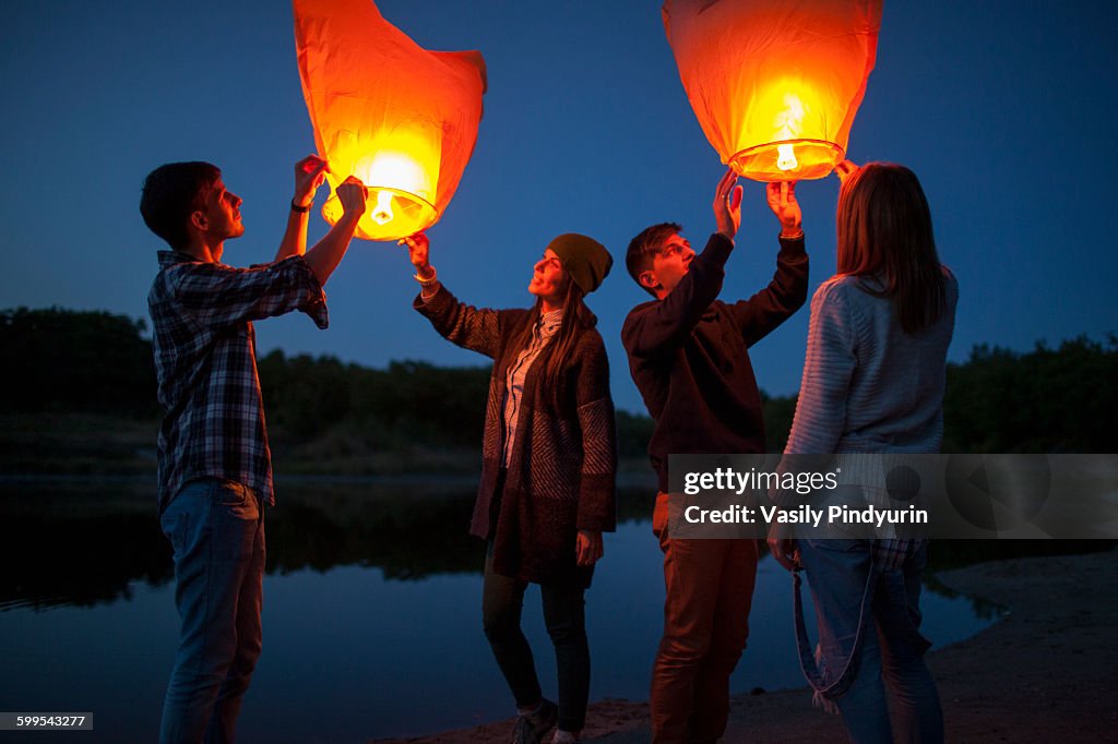 Male and female hikers releasing paper lanterns at lakeshore