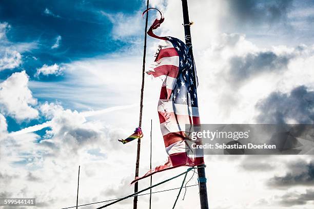 tattered american flag on pole against cloudy sky - frayed stock-fotos und bilder