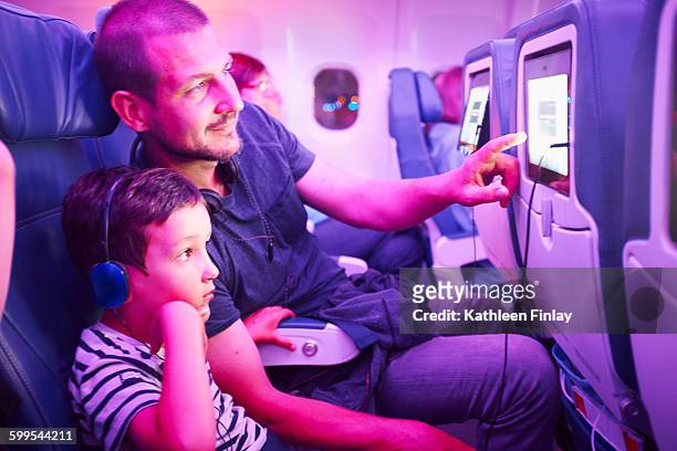 father and son sitting in aeroplane, looking at in-flight tv screen - kunst cultuur en vermaak stockfoto's en -beelden