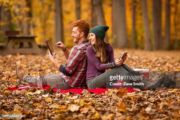 young couple back to back using digital tablet and smartphone in forest - man lady phone ipad outside stock pictures, royalty-free photos & images