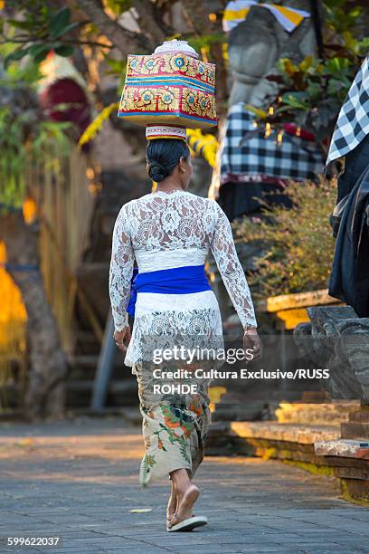 woman walking towards temple, carrying offering on head, rear view, bali, indonesia - bali women tradition head stock pictures, royalty-free photos & images
