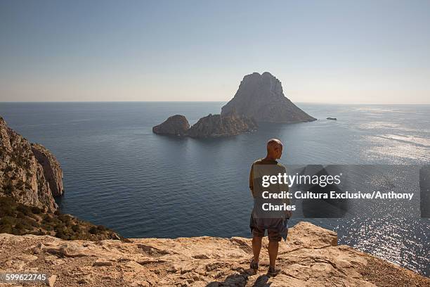 mid adult male tourist looking out to es vedra from cliff, ibiza, spain - es vedra stock pictures, royalty-free photos & images