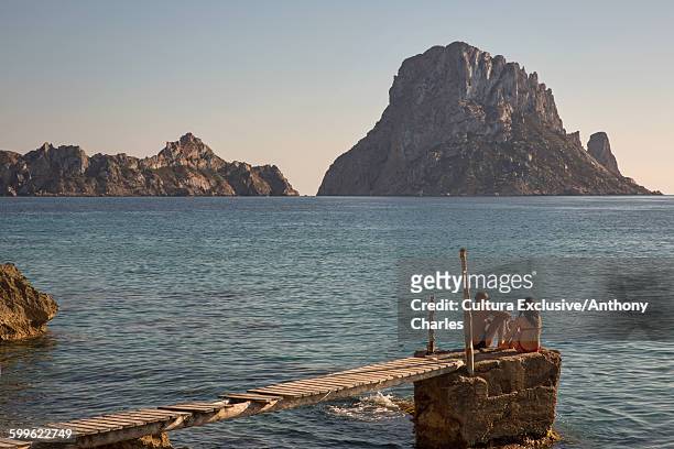 tourist couple sitting on pier looking over to es vedra, ibiza, spain - es vedra stock pictures, royalty-free photos & images