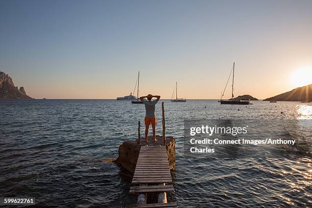 young man standing on old pier at sunset, ibiza, spain - anchored stock pictures, royalty-free photos & images