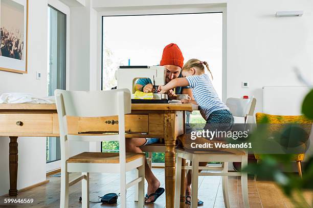 father and daughter at home using sewing machine - rolwisseling stockfoto's en -beelden