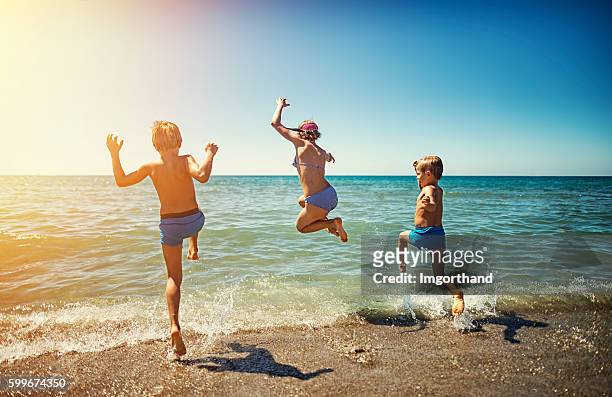 summer vacations in italy - kids jumping into the sea - jumping for joy stockfoto's en -beelden