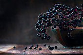 Black elderberries (Sambucus nigra) in a bowl, dark rustic wood