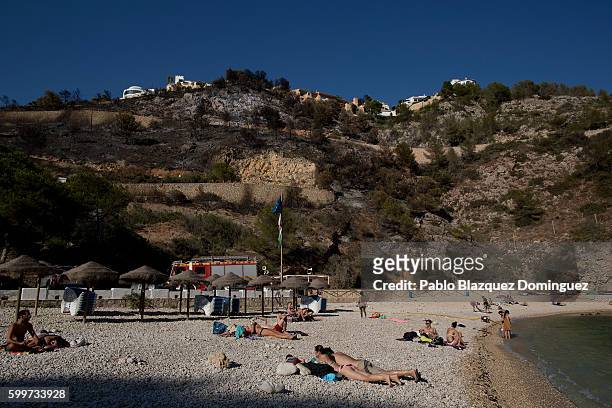 People sunbathe in the beach as burned areas are seen on the back at Granadella Beach on September 6, 2016 in Javea, in Valencia province, Spain....