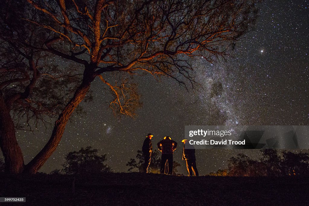 Three men standing by a campfire under the Milky W