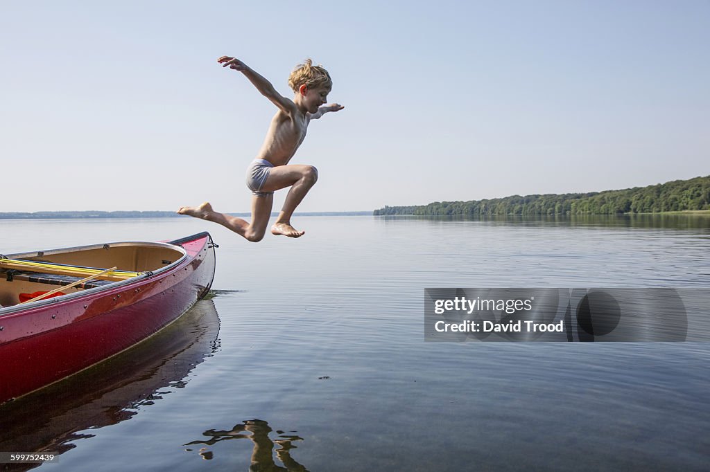 Seven year old boy jumping from a canoe.
