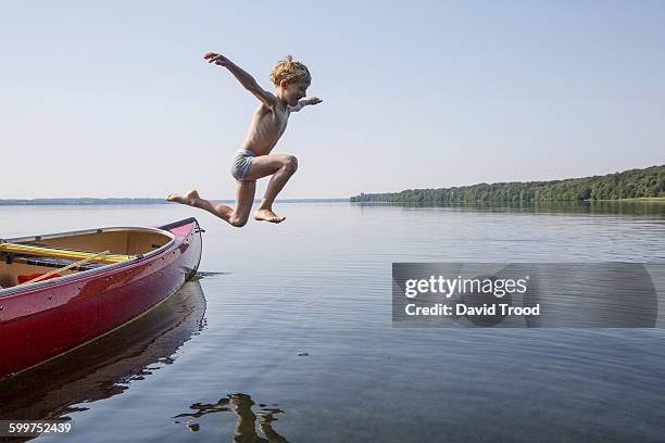 seven year old boy jumping from a canoe. - summer denmark stock pictures, royalty-free photos & images