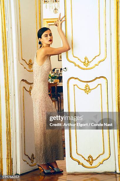 Model, Trish Goff, poses in grand doorway, her arm resting on the gold trimmed door; she wears a white beaded dress by Giorgio Armani; her hair is...