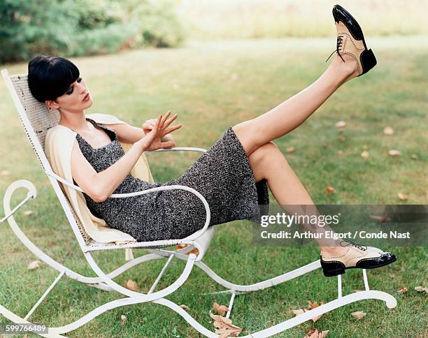 Model, Stella Tennant, wearing a sleeveless shift in black-and-white bouclé tweed, by Gianni Versace, with a white cashmere cardigan over her...