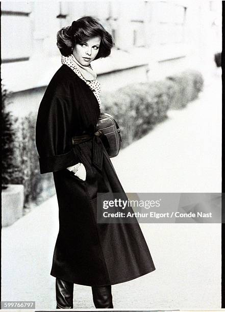 Model Lisa Taylor, holding a leather bag, and wearing a dark wool kimono coat, and polka dot shirt and scarf, alll by Yves Saint Laurent CREDIT MUST...