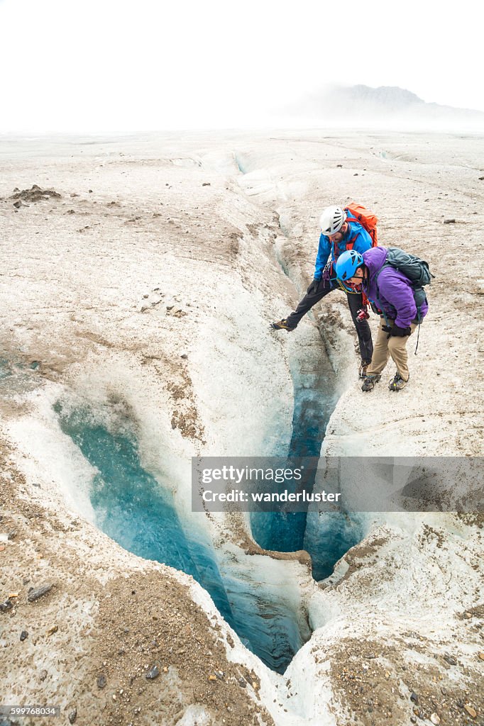 Guide and senior woman peer into glacier moulin