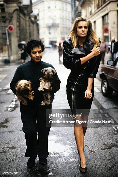 Fashion designer Azzedine Alaia holding his two Yorkshire terriers, Patapouf and Wabo, walking in Paris street with model Frederique who wears one of...