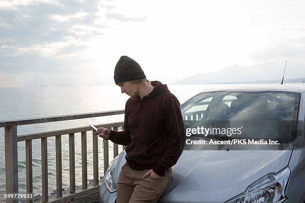 man relaxes against car above sea, texting - brown pants foto e immagini stock