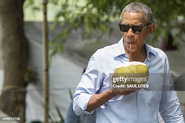 President Barack Obama drinks from a coconut as he makes a surprise stop for a drink alonside the Mekong River in Luang Prabang on September 7, 2016....