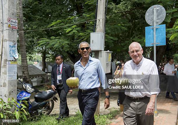 President Barack Obama drinks from a coconut with the US Ambassador to Laos Daniel Clune as he makes a surprise stop for a drink alongside the Mekong...