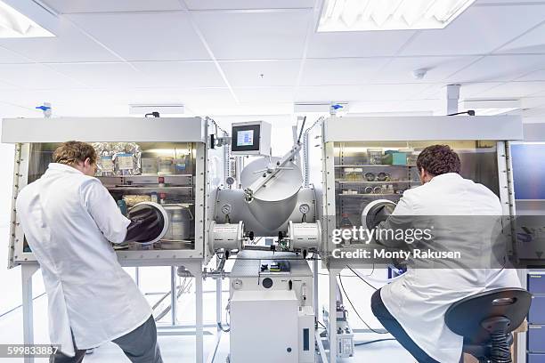 scientists assembling lithium ion test batteries in glove chamber in battery research facility - lithium ion battery stock pictures, royalty-free photos & images