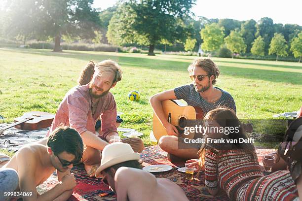 group of friends relaxing on rug at sunset park party - party food and drink stock pictures, royalty-free photos & images