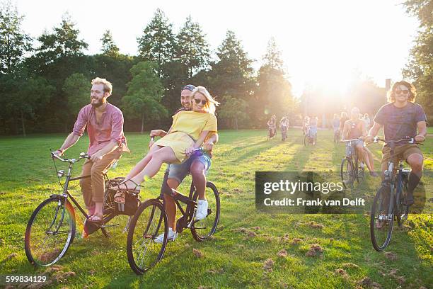 crowd of partygoing adults arriving on bicycles to sunset park party - friends cycling stock pictures, royalty-free photos & images