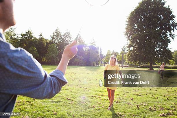 young couple playing badminton in sunlit park - badminton stock-fotos und bilder