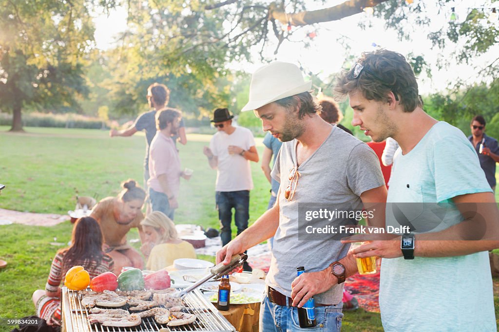 Young men barbecuing at group party in park