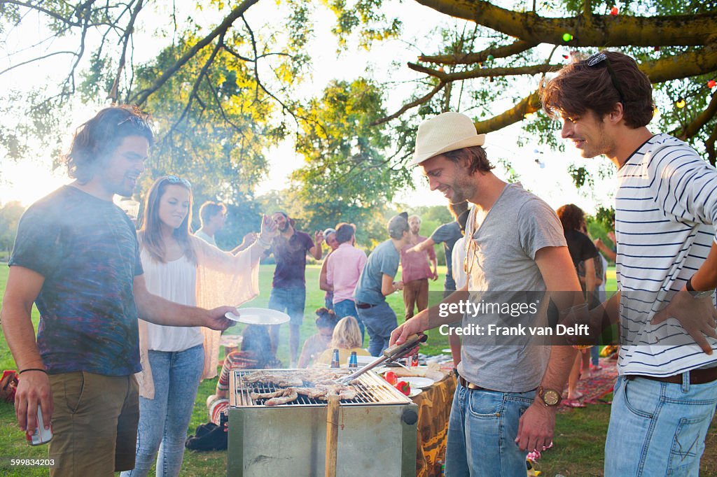 Happy adult friends barbecuing at sunset party in park