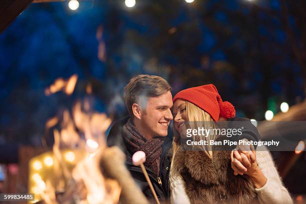 romantic young couple toasting marshmallows at xmas festival in hyde park, london, uk - christmas scenes stock pictures, royalty-free photos & images