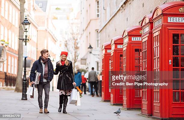 young shopping couple strolling past red phone boxes, london, uk - british culture walking stock pictures, royalty-free photos & images