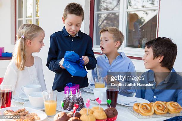 boy with siblings unwrapping birthday gifts on patio - open 2015 day 7 stockfoto's en -beelden