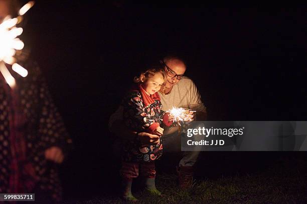 father crouching next to daughter holding sparkler - family fireworks stockfoto's en -beelden