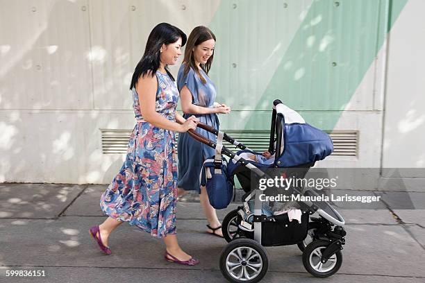 young woman and mother and pushing baby carriage along street - femme poussette rue photos et images de collection