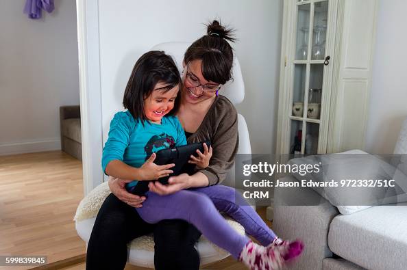 A small girl playing on an electronic tablet with her mother in an arctic village home.