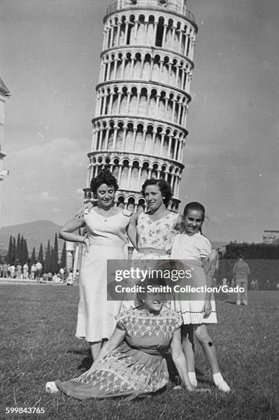 Mother, daughters and grandmother posing in front of the Leaning Tower of Pisa, reclining on a lawn, other tourists visible in the background, Pisa,...