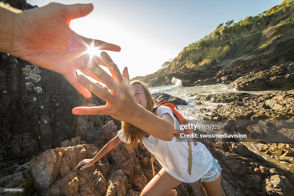Girl climbs on cliff, partner pulls out hand for assistance