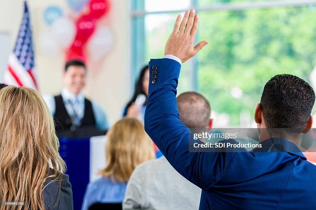 Hispanic man raising hand during political town hall meeting
