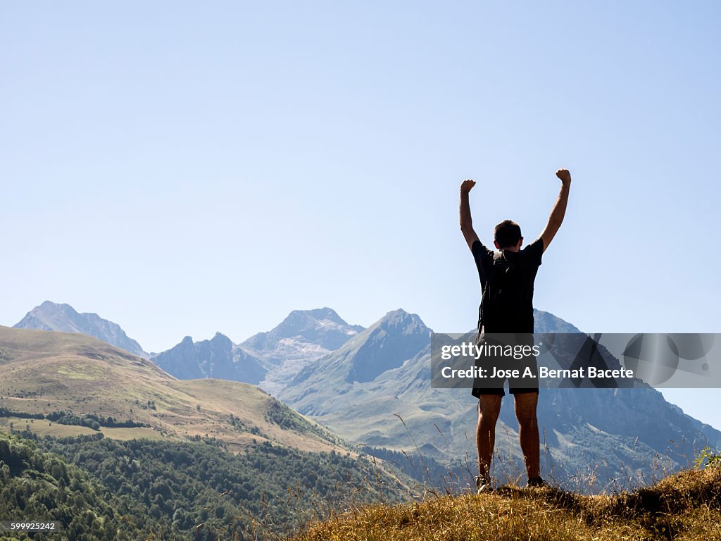 Man on top of a mountain with arms outstretched as a symbol of victory