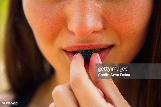 beautiful caucasian girl biting and eating a blackberry fruit with sensual lips and mouth with close up detail. - flushing stock pictures, royalty-free photos & images