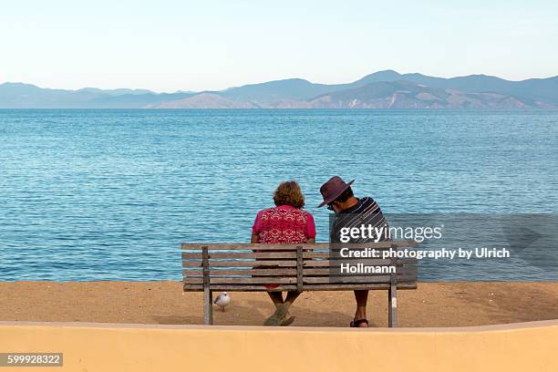 senior couple sitting on bench at waterfront - kaiteriteri stock-fotos und bilder
