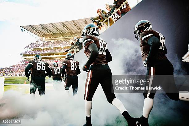 fans cheering football team running out of tunnel - american football stadium stock pictures, royalty-free photos & images
