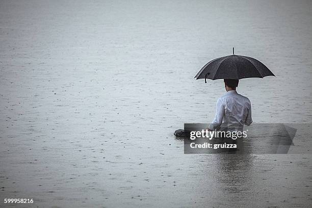 bel homme debout dans l’eau et tenant le parapluie pendant la pluie - pluie diluvienne photos et images de collection