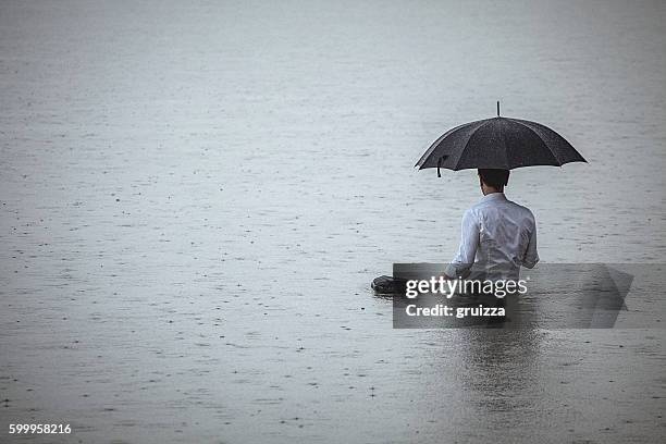 bell'uomo in piedi in acqua e tenendo l'ombrello durante la pioggia - meteo estremo foto e immagini stock